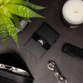 Photo of a black Tempest RFID Wallet with elasticated band and backplate laid on a table next to sunglasses, a key organiser and plant