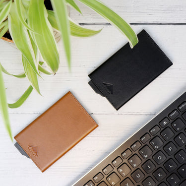 Picture of 2 Wrapped Avenger RFID Wallets laid out on a desk, next to a plant and computer keyboard